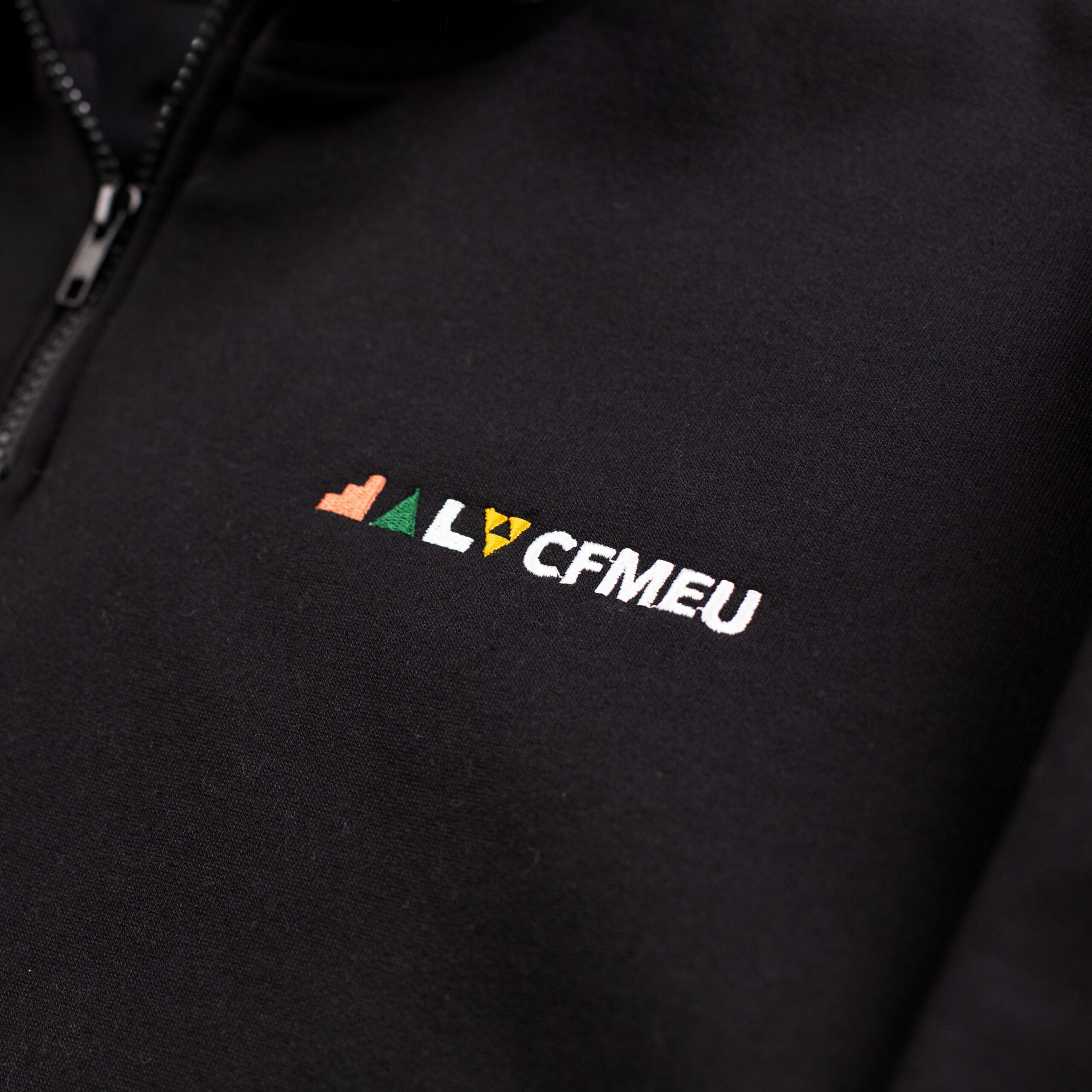 Close-up of black fabric with a zipper on the left and multicolored embroidery spelling HELLO partially shown.