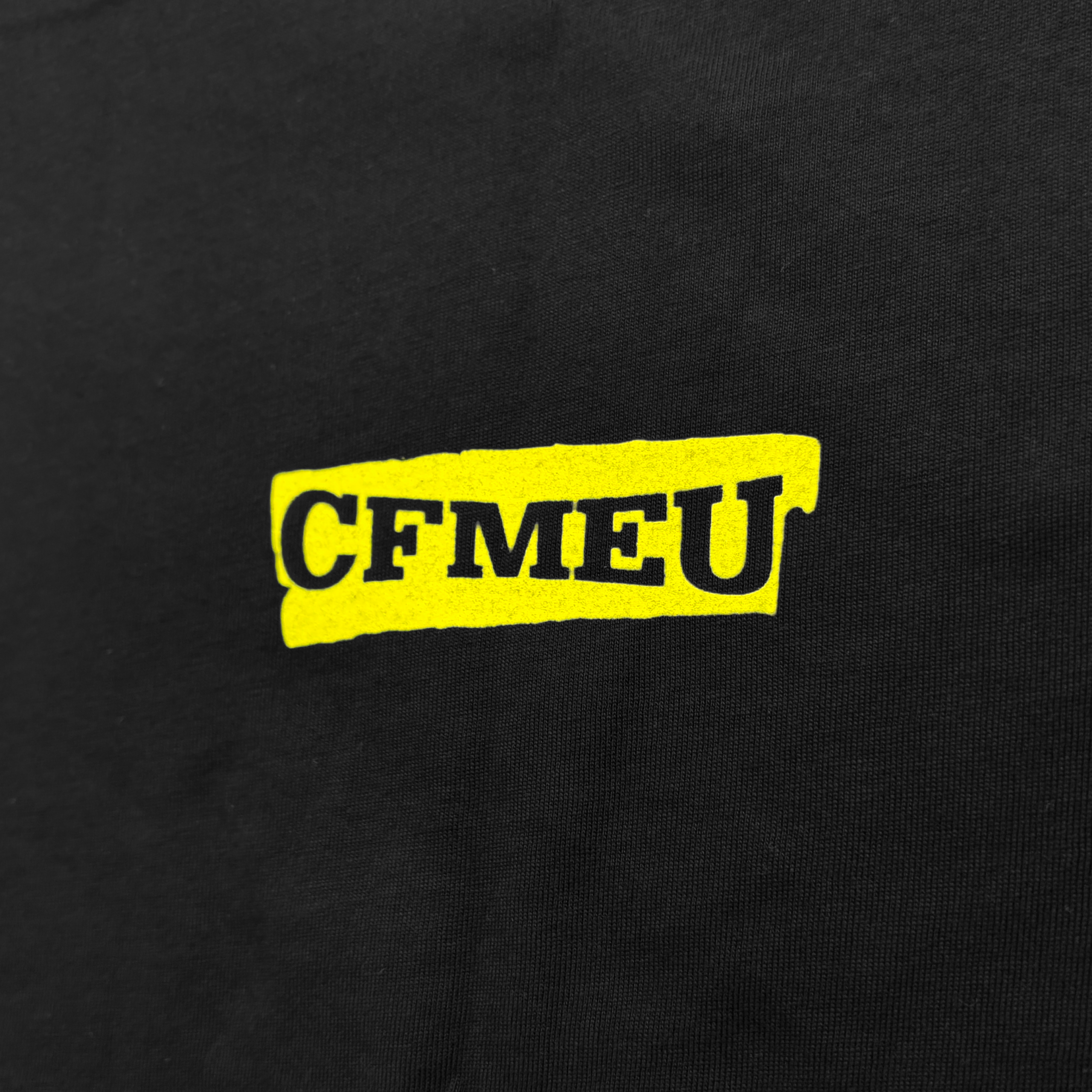 Close-up of black fabric with a bright yellow rectangular graphic containing bold black lettering (partially visible).